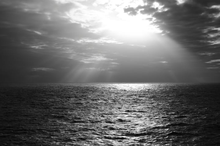 Sunrays through a cloudy overcast over a dark ocean.